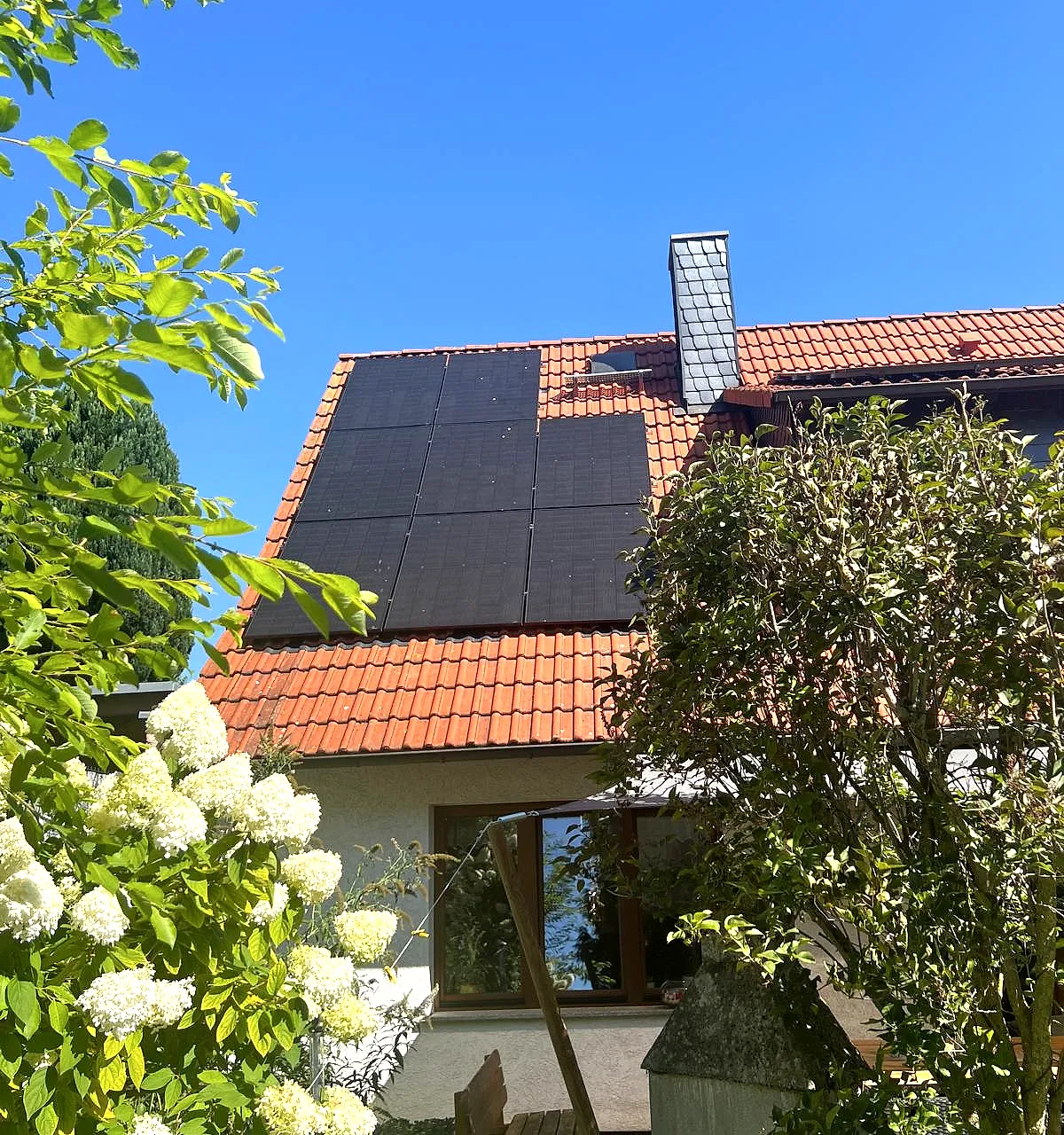 Photovoltaikmodule auf einem Ziegeldach, im Vordergrund ein blühender Garten