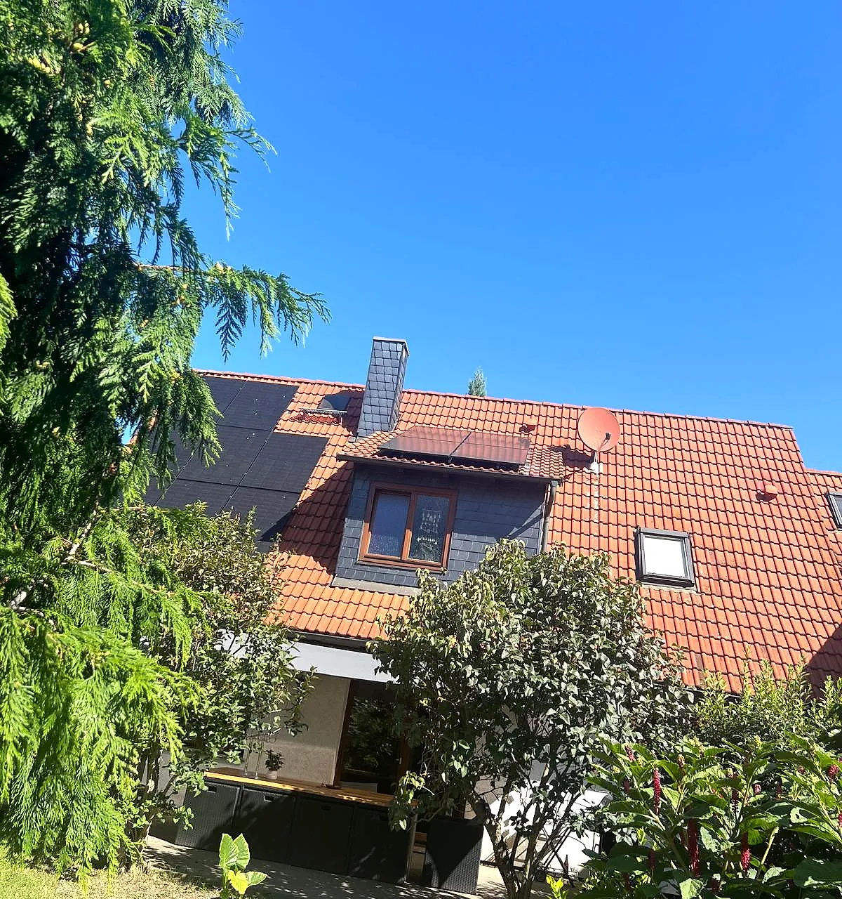 Wohnhaus mit Photovoltaikanlage, umgeben von Bäumen und Garten