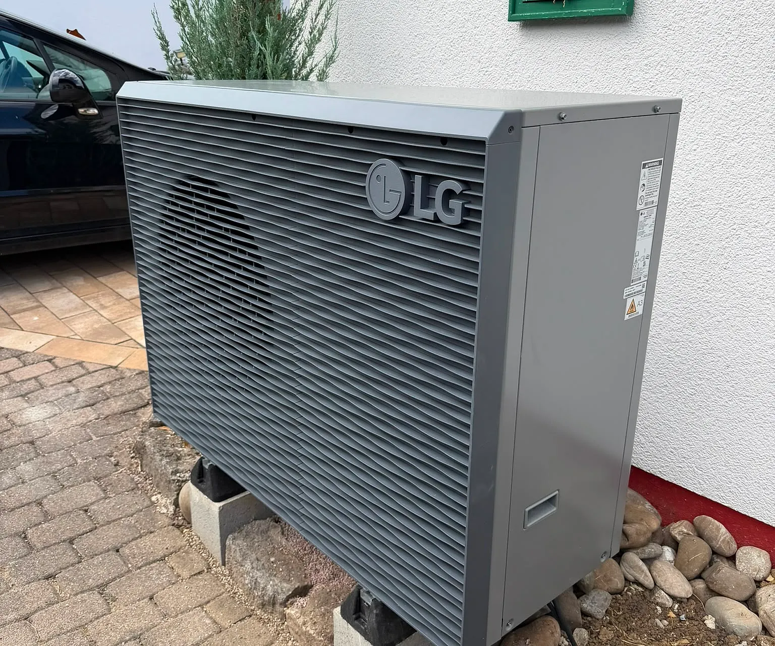 Außeneinheit einer Wärmepumpe auf Betonsockeln neben einem Wohnhaus